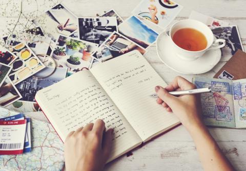 person writing in a journal with a tea cup to the side